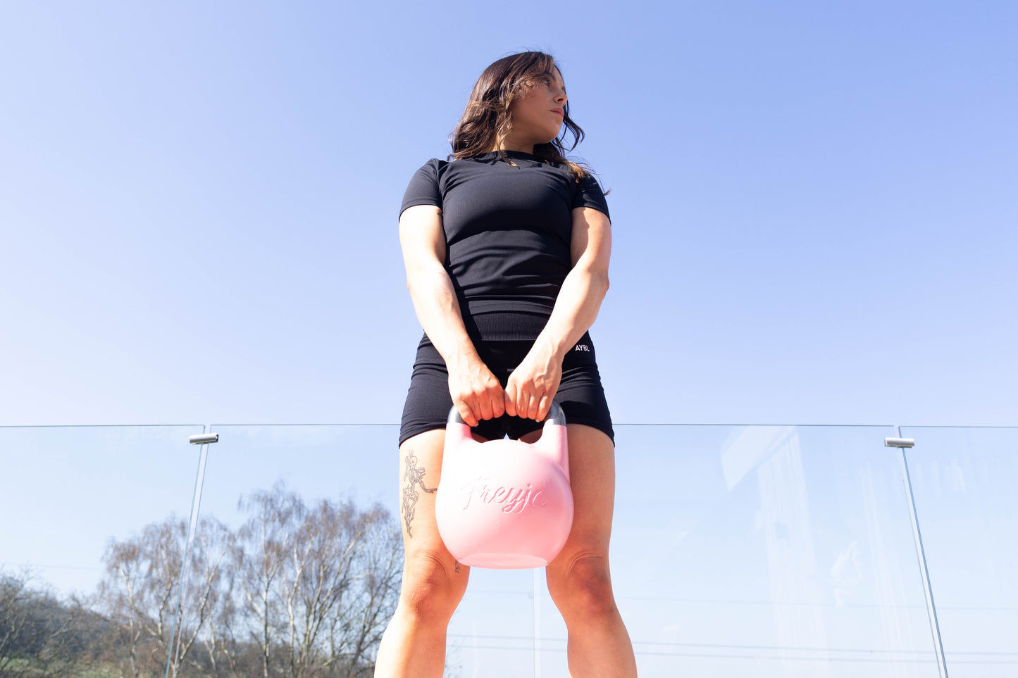 Woman holding a pink Freyja Fit kettlebell outdoors on a clear, sunny day