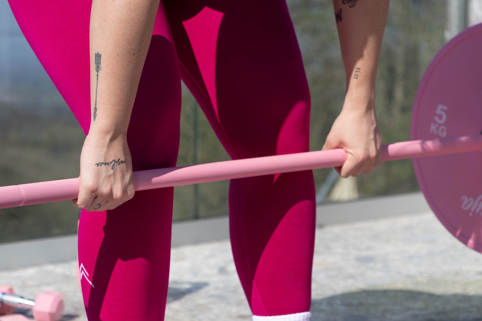 Woman lifting a pink Freyja Fit barbell with weights outdoors