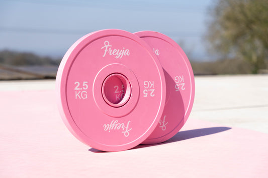 Two Freyja Fit pink change plates on a pink yoga mat with a blurred outdoor background