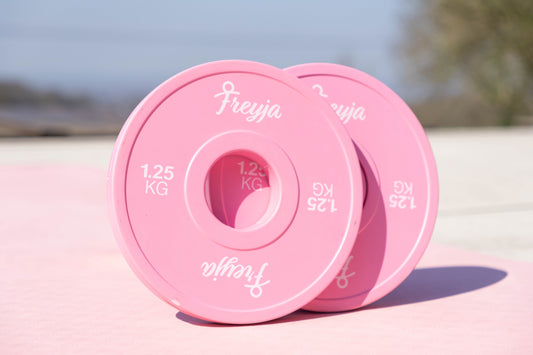 Two Freyja Fit pink change plates on a pink yoga mat with a blurred outdoor background