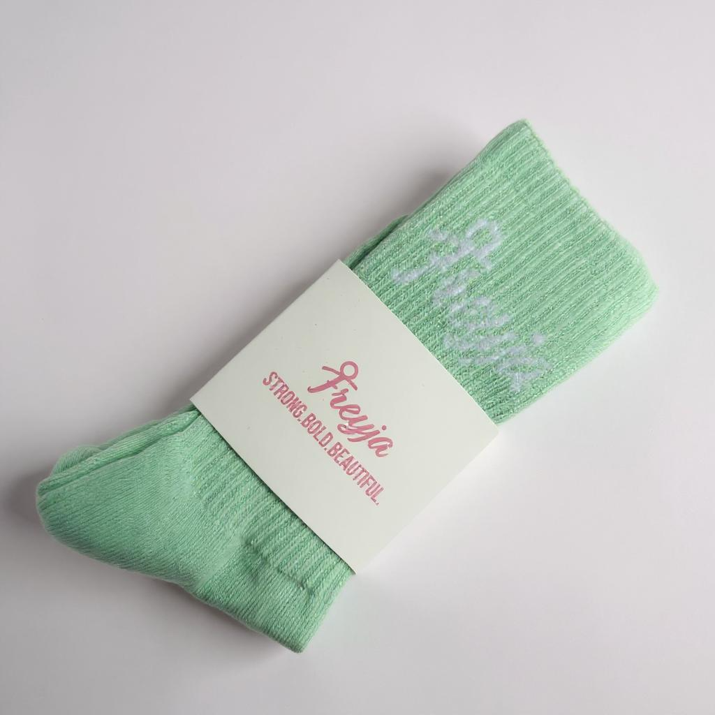 Green freyja branded socks with a white label on a light grey background