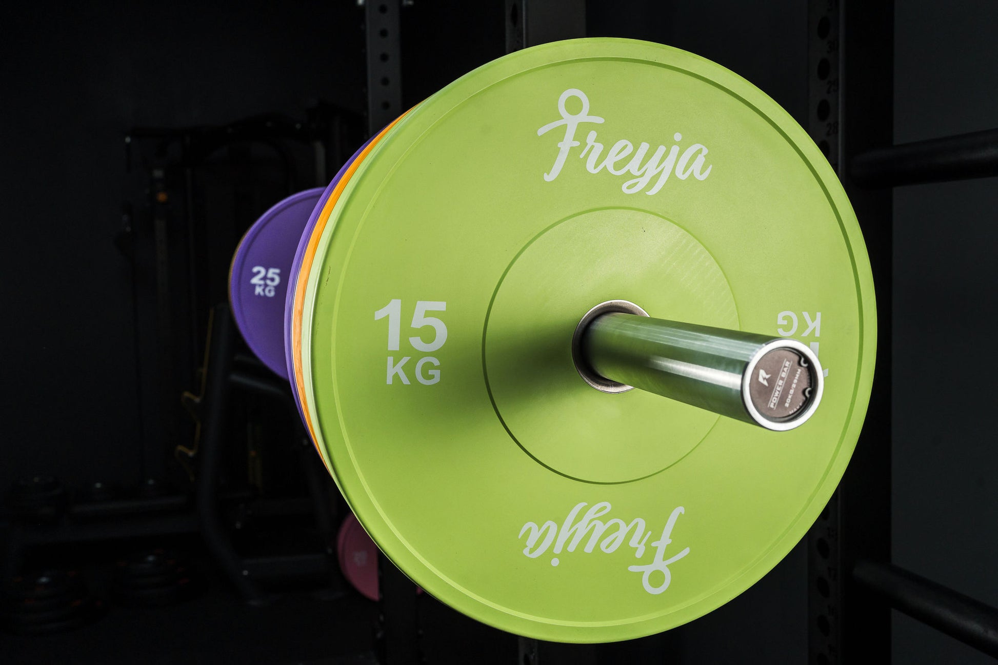 Green Freyja Fit weight plate on a black squat rack in a gym
