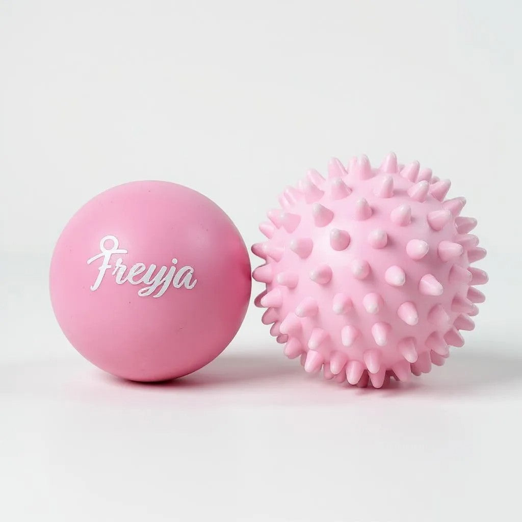 Two Freyja Fit pink massage balls, one smooth and one with a textured surface, displayed on a light grey background