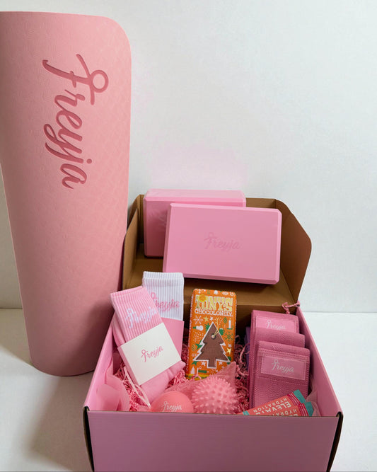 Pink fitness gift set with yoga mat, blocks, socks, and massage ball in branded packaging