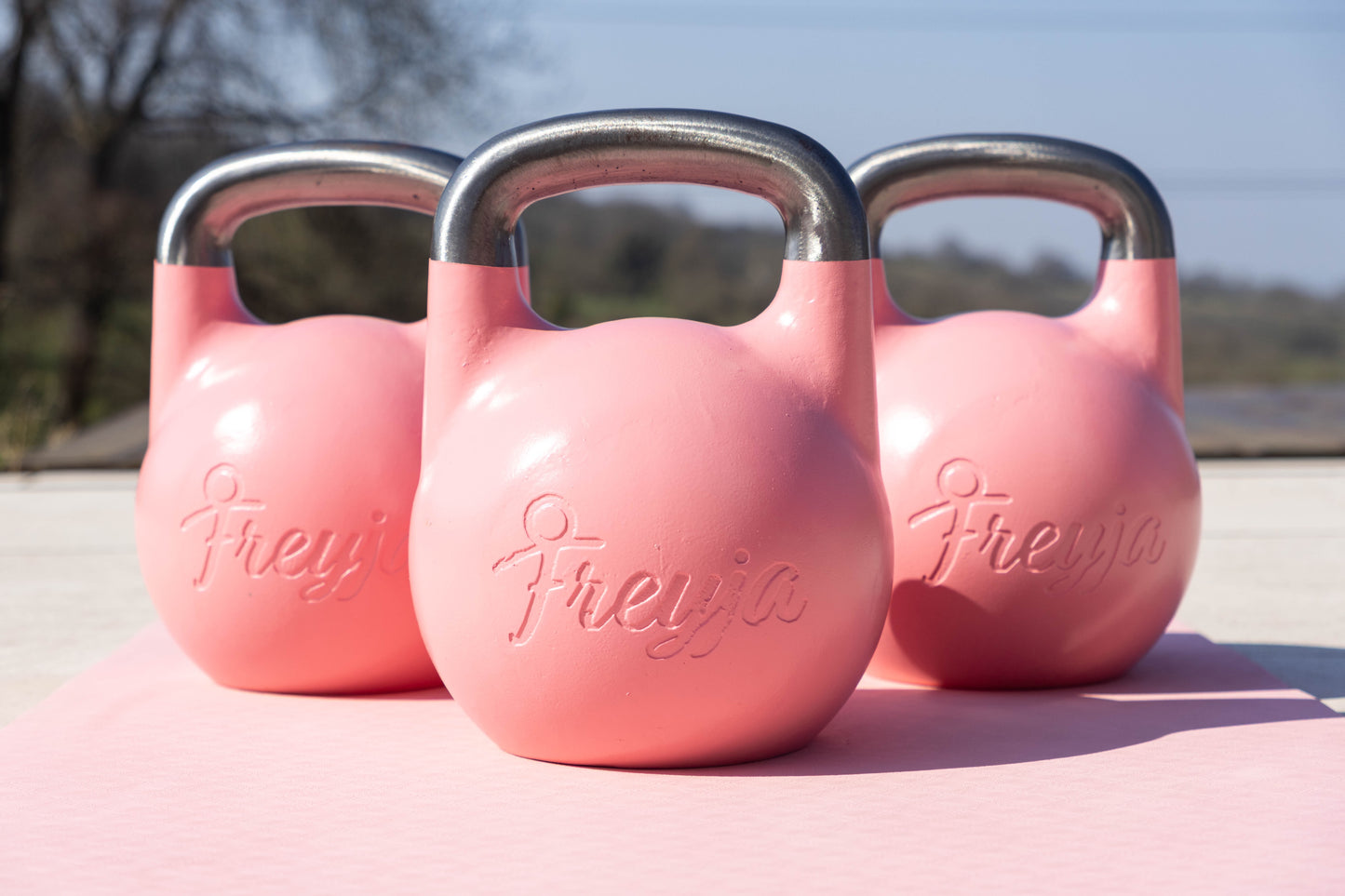 Three pink Freyja kettlebells on a pink Freyja yoga mat on a concrete surface