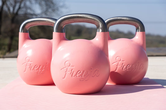 Three pink Freyja kettlebells on a pink Freyja yoga mat on a concrete surface