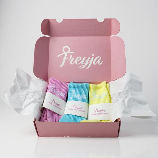 Pink box with Freyja branding containing pastel colourful socks on a light grey background