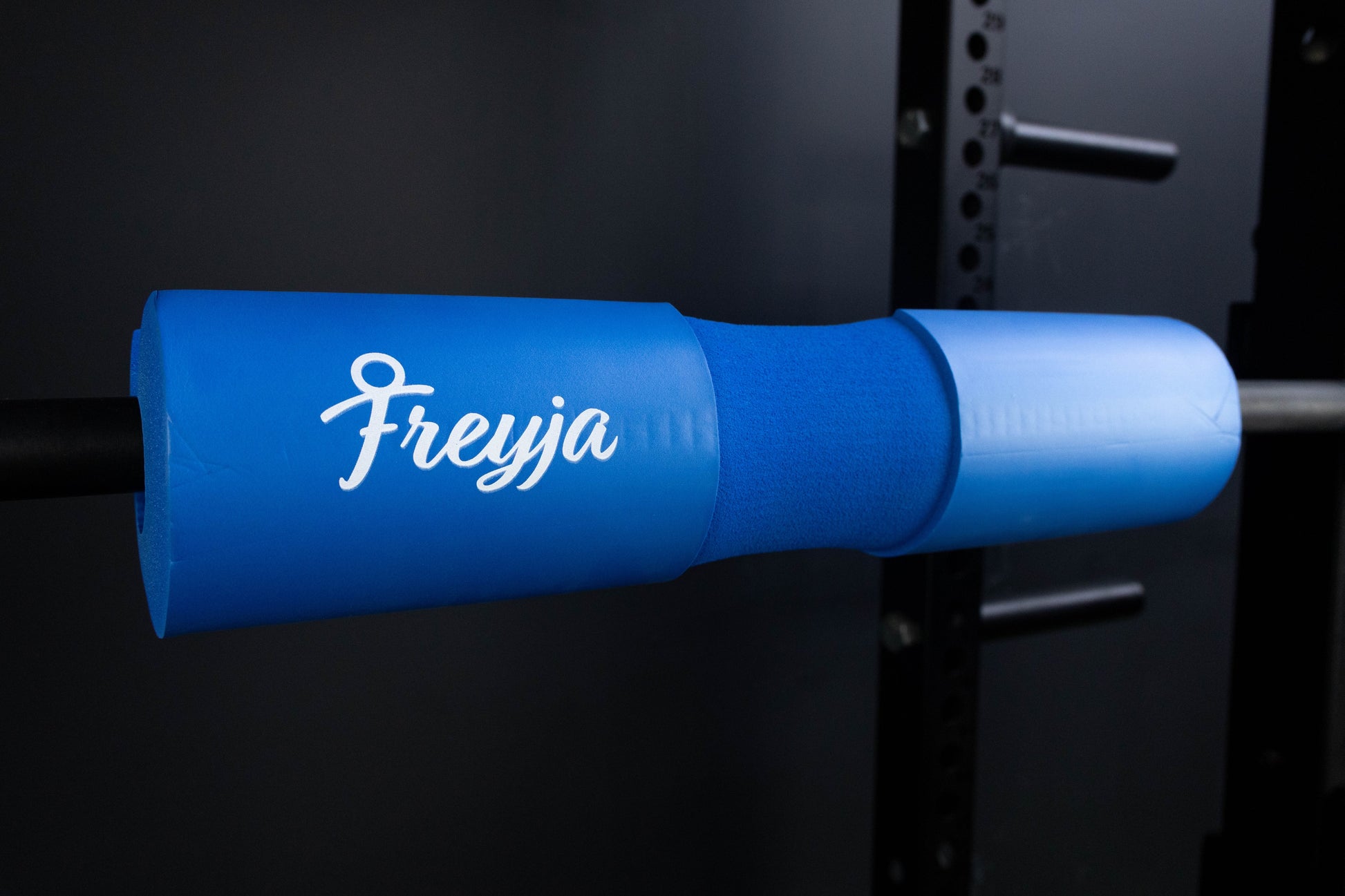 Blue foam freyja barbell pad on a black barbell in a gym setting 