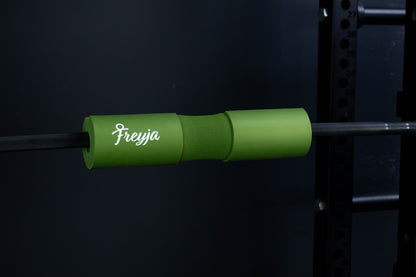 Green freyja foam barbell pad on a black barbell in a gym setting 