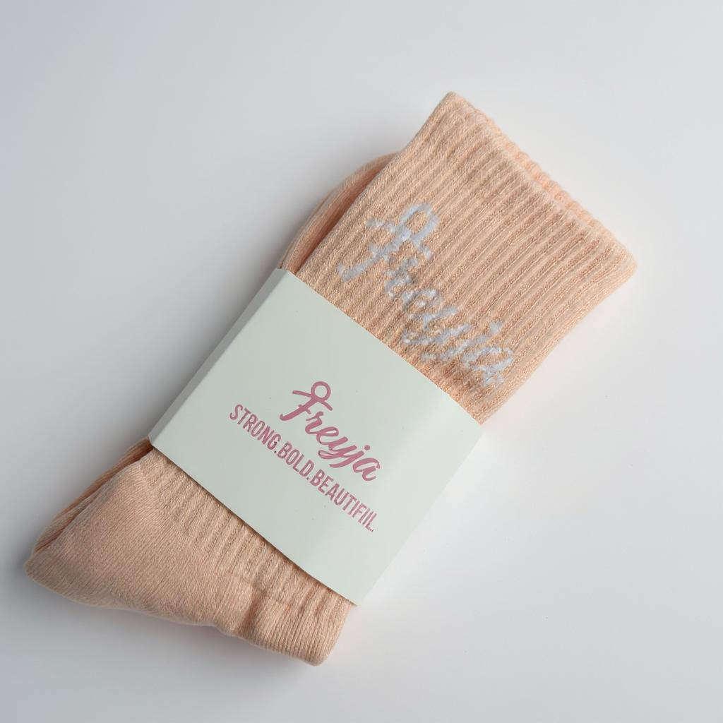 Pair of freyja branded peach socks with a label on a light grey background