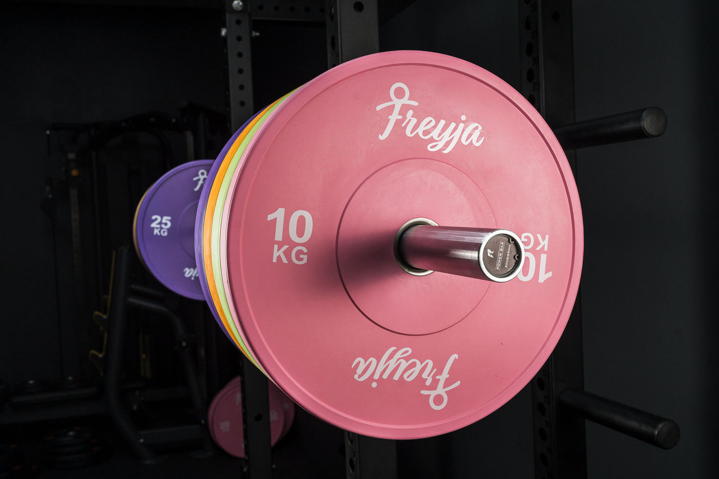 Close-up of a pink Freyja Fit bumper plate on a barbell against a black background