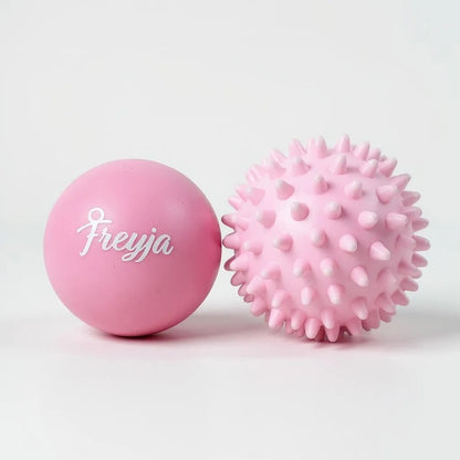 Two Freyja Fit pink massage balls, one smooth and one with a textured surface, displayed on a light grey background