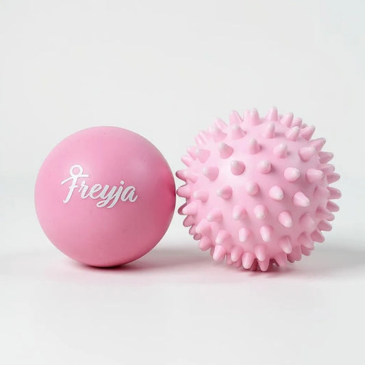 Two Freyja Fit pink massage balls, one smooth and one with a textured surface, displayed on a light grey background