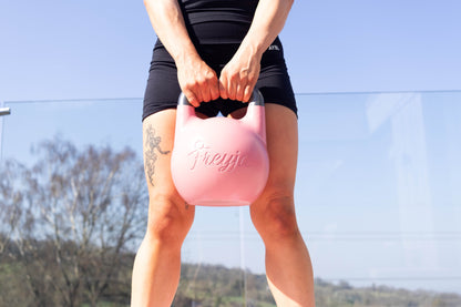 Outdoor shot of a woman holding a pink Freyja kettlebell under a clear sky