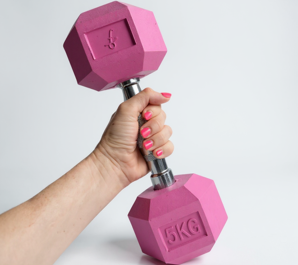 Close-up of a hand holding a pink 5KG Freyja Fit dumbbell against a light grey background