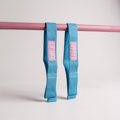 Blue freyja lifting straps with pink labels hanging on a pink bar against a light grey background