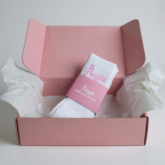 Freyja Fit branded socks in a pink box, showing white socks with a pink label, displayed on a light grey background.