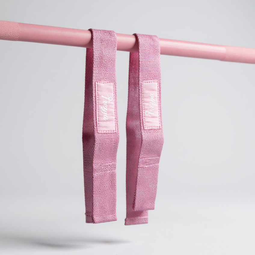 Pink freyja lifting straps hanging on a pink barbell with a white background