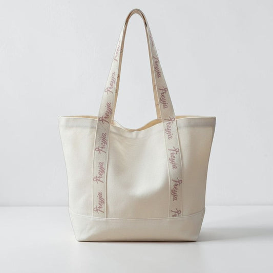 Beige tote bag with embroidered pink text on straps 