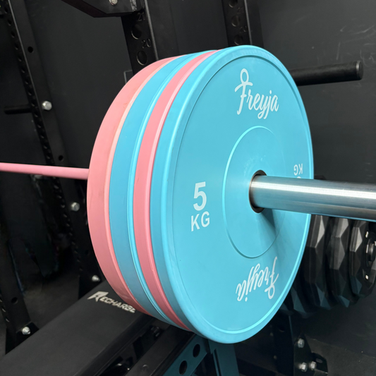 Blue and pink weight plates on a barbell with 'Freyja' branding against a gym background.
