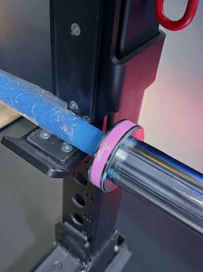 Close-up of a 7.5kg blue technique barbell with pink collar, secured on a black rack for weightlifting practice.