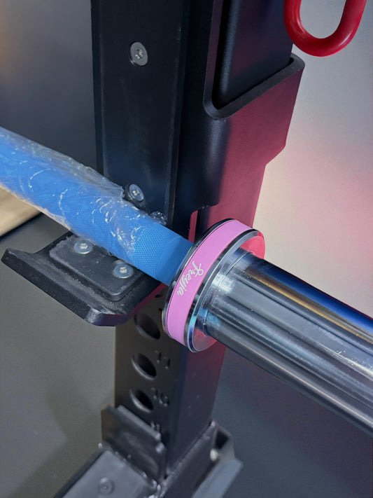 Close-up of a 7.5kg blue technique barbell with pink collar, secured on a black rack for weightlifting practice.